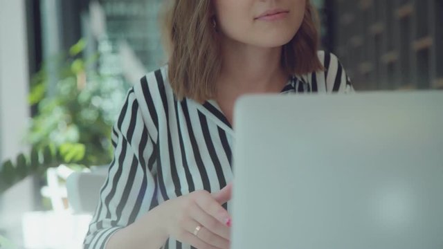 Smart modern woman working in cafe with gadgets - laptop and smartphone. Lifestyle - young woman, 20-25 years old sitting in light room with plants on the background and surfing in internet.