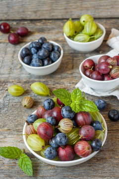 Summer gooseberry and blueberry berries in a plate on a wooden rustic background.