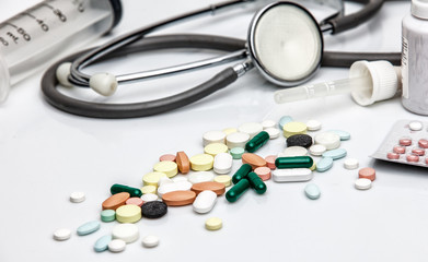 Pills, syringe and phonendoscope against white background