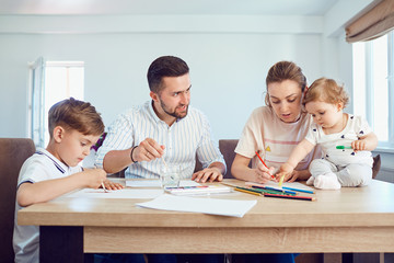 Happy family draws paints on a paper at the table in the room.