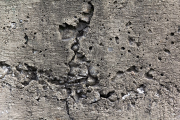 Porous with small cracks gray concrete wall, with protruding pebbles from the inside