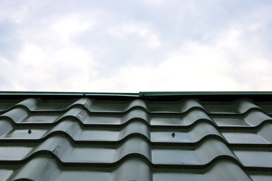 New green roof of house made of iron shingles against blue sky background closeup