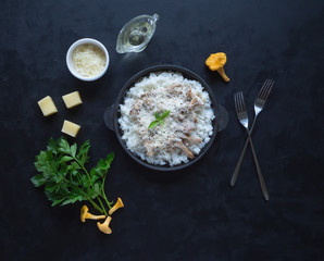 Risotto of chanterelles in a cast iron pan on a black table.
