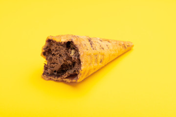 chocolate flavor ice cream cone with the last bit on a yellow background