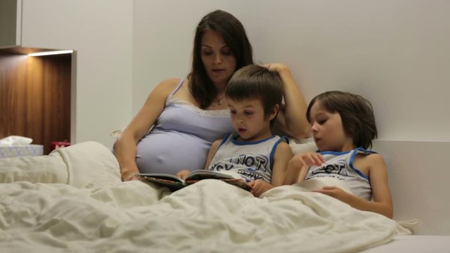 Pregnant mum, reading bedtime story for her sons