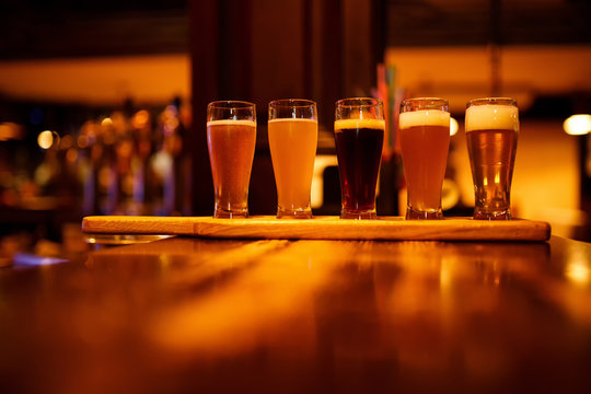 Various types of craft beer in small glasses on a wooden table in a pub.
