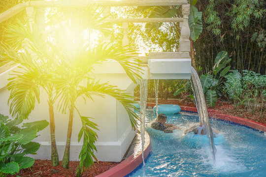 Lazy River Pool With Waterfall. People Have Fun With River Run Inflatable Floating Tube Water Raft During Vacation In Resort.