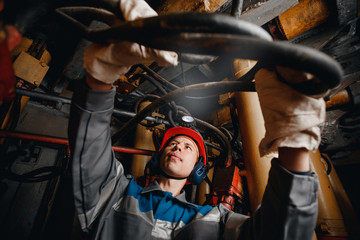 Young miner man underground in mine for coal mining overalls is busy with work, repairing against...