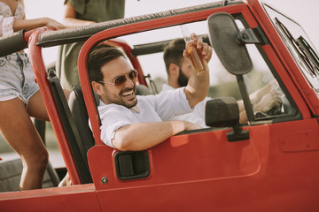 Naklejka premium Group of young happy people enjoying road trip in red convertible
