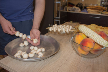 A man hand puts pieces of mushrooms on skewer. mushrooms on skewers