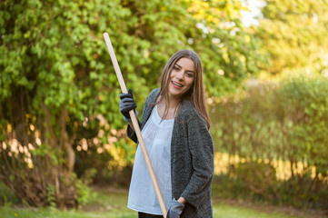 Smiling young woman with garden hose watering her home backyard with flowers, plants and vegetation. Gardening as hobby and leisure concept.