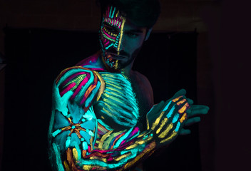 Young man painted in fluorescent paint on face and muscular torso, in studio shot with UV light