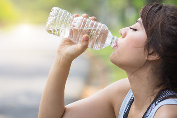 Sport woman drinking water bottle after exercise..Young Asian girl thirsty after jogging training..Fitness lady drinking fresh water after intense workout..Athlete female exercising in park outdoors.