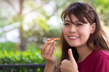 Young woman eating delicious pizza showing excellent hand sign. Asian girl making thumb up for good pizza.