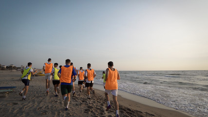 Durres, Albania - circa August, 2017: Football sport team is engaged in jogging training at sea at sunrise. Thay make a run along the sea coast. steadicam shot