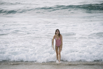 Fototapeta na wymiar Portrait of a surfer woman on a beach holding a surfboard