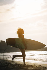 Fototapeta na wymiar Woman with surfboard standing on wet sandy beach at the ocean.