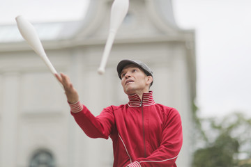 A man in a cap juggles with clubs on the street of a European city