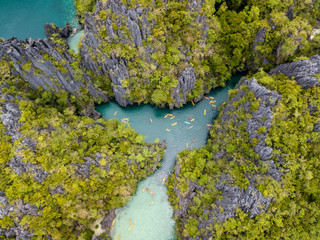 Naklejka na ściany i meble Aerial drone view of kayaks inside a beautiful lagoon surrounded by towering limestone cliffs (El Nido, Philippines)