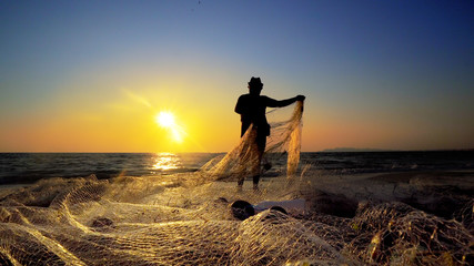 Silhouette of traditional fishermens pulling net fishing at ocean coast at sunset - obrazy, fototapety, plakaty