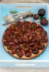 Sweet pie from short pastry with caramelized plums and ripe plums on a wooden table. Rustic style.