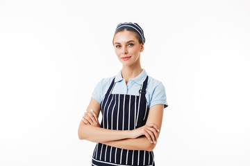 Beautiful woman cook in striped apron and cap dreamily looking in camera with arms folded over white background