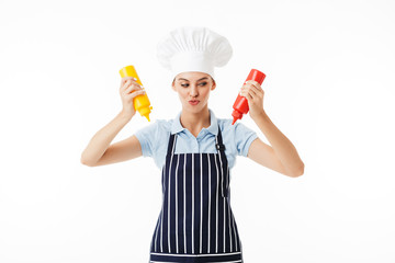 Young cunning woman cook in striped apron and white hat thoughtfully looking aside while holding...
