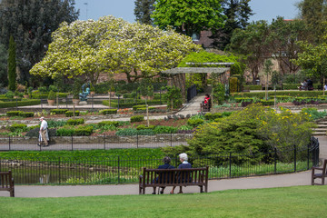 Golders Hill Park, London, UK - May 7th 2013: A couple of people sitting on a wooden bench in front of a garden and pond.