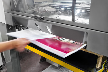 polygraphic process in a modern printing house, print operator pulls printed sheet of paper