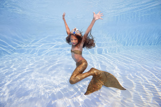 A girl in a mermaid costume poses underwater in a pool