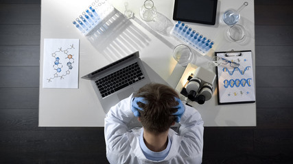 Disappointed laboratory worker sitting upset by experiment failure, top view