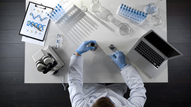 Lab assistant checking oil product in flask, making chemical mixture, top view
