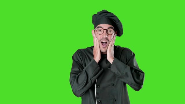Shocked young chef posing against green background