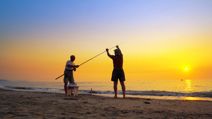 Fototapeta na wymiar Silhouette of active fishermans fishing with rod at summer sea sunset