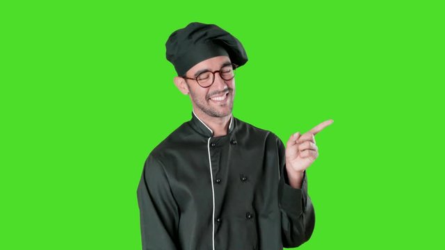 Happy young chef pointing with his finger against green background
