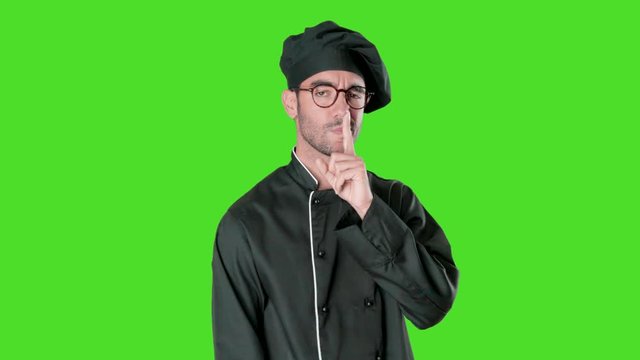 Serious young chef with a silence gesture against green background