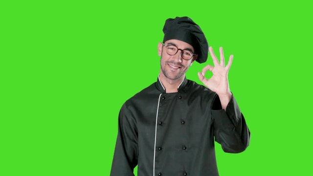 Satisfied young chef with a gesture of all right against green background