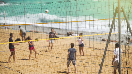 Young active people playing volleyball on sandy beach, team sport for friends