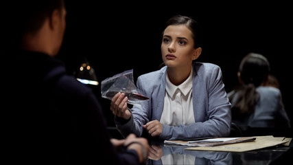 Attractive lady interrogator demonstrating bloody knife evidence to suspect