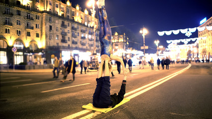 Woman and man doing acrobatic stunts in city center, evening time, extreme hobby