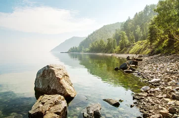 Foto op Canvas Landschap van de oever van het meer met rotsen en bergen op de achtergrond © vika33
