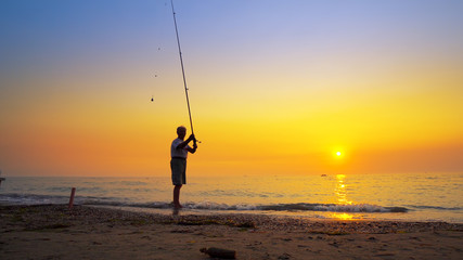 Silhouette of an active fisherman throwing fishing tackles at sea sunset