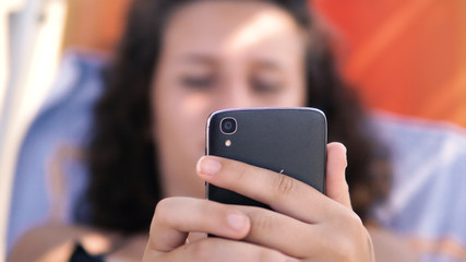 Female teen play games on smartphone during summer holidays lying on beach bed, cinematic selective focus dof