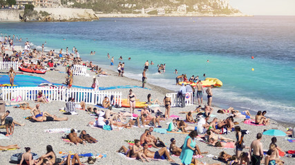 Crowded public beach at seashore, many people sun tanning, splashing in water