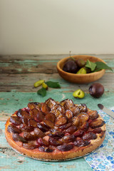 Sweet pie from short pastry with caramelized plums and ripe plums on a wooden table. Rustic style.