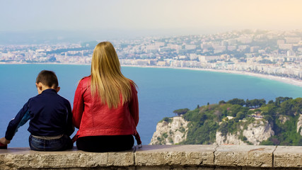 Mother and little son sitting on stone bench and enjoying fantastic view of city