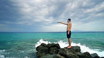 Fototapeta na wymiar Lost alone male teen standing on sea rock and navigating horizon