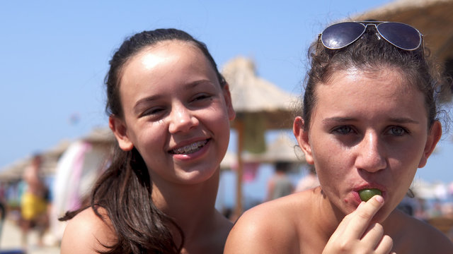 Authentic image of two smiling girls on beach eating green grapes, cinematic selective focus dof