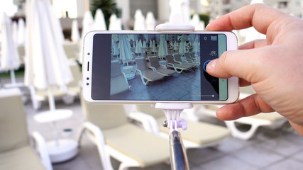 A blogger on vacation makes a photo using a smartphone. A man takes pictures of sun beds and umbrellas by the pool.