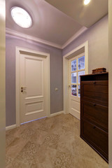 White doors, a dark dresser, a floor tile and lilac walls in a corridor